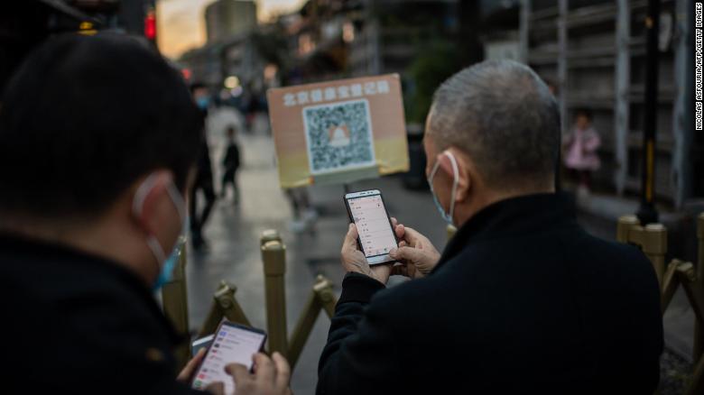 People wearing face masks scan a QR code with their smartphones to check their &quot;Health Kit&quot; to enter an area in Beijing this week.