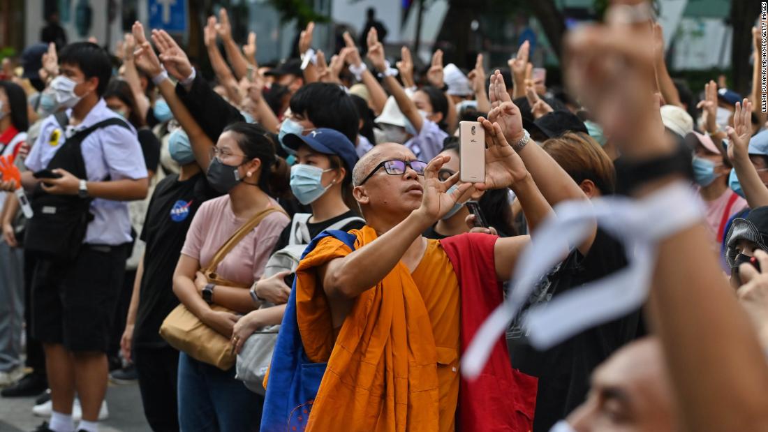 A monk takes photos with his mobile phone as protesters give the three-finger salute on October 15.