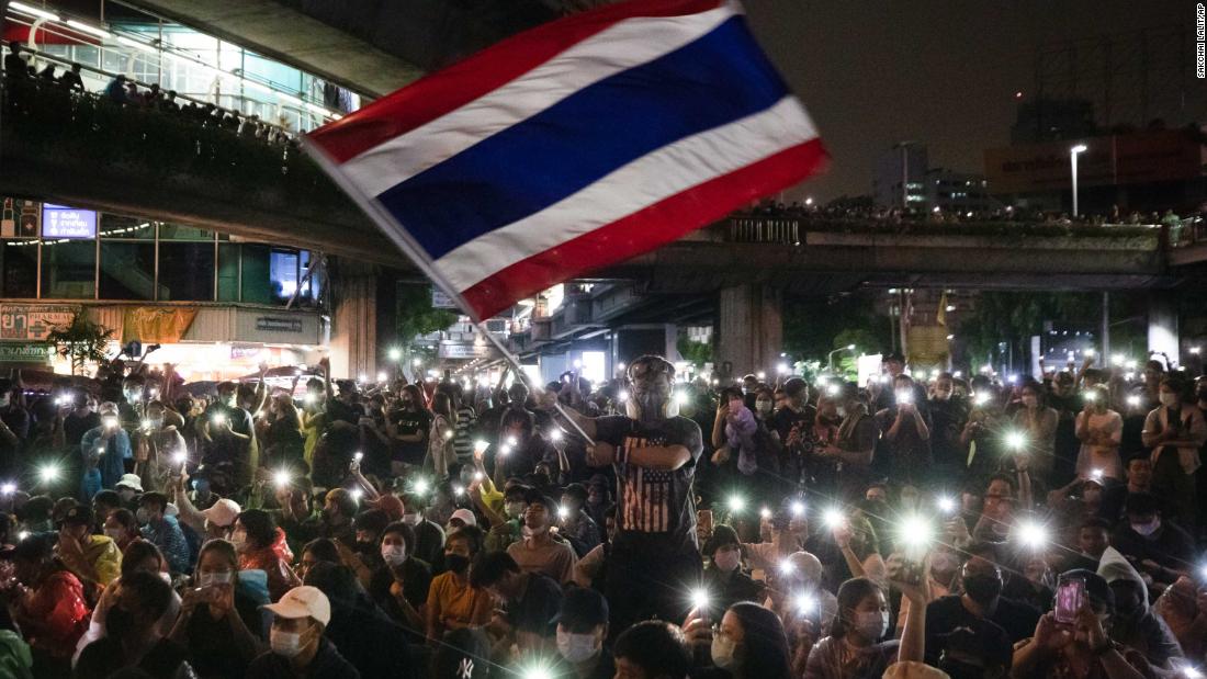 A protester waves Thailand&#39;s national flag as others shine their mobile phone lights on October 18.