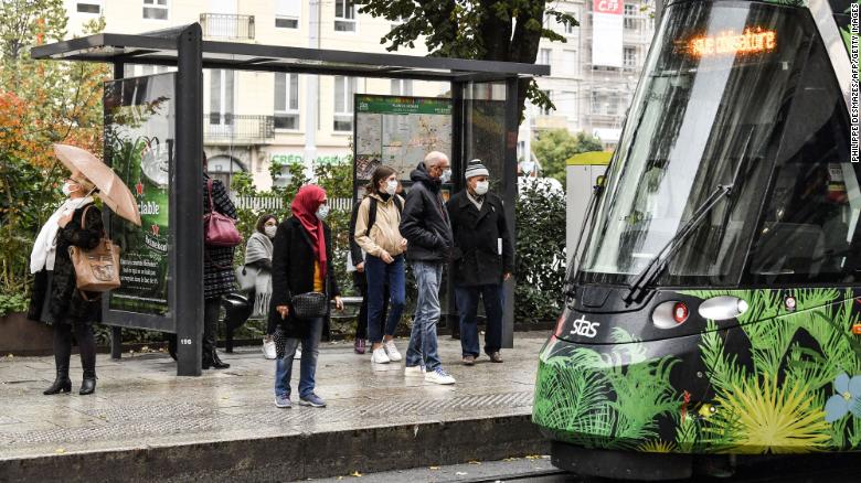 People wearing protective face masks  wait for a tram on October 22, 2020 in a street of Saint-Etienne, central eastern France. 