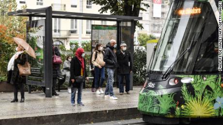 People wearing protective face masks  wait for a tram on October 22, 2020 in a street of Saint-Etienne, central eastern France. 