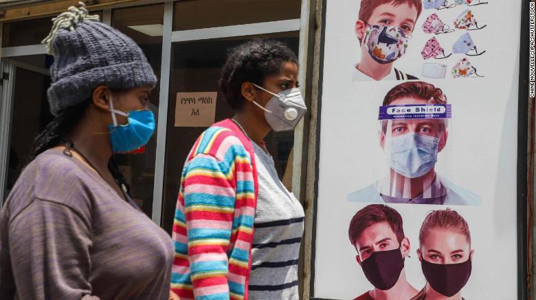 People wearing face masks walk past a poster promoting the use of face mask and face shield in Addis Ababa on August 21.