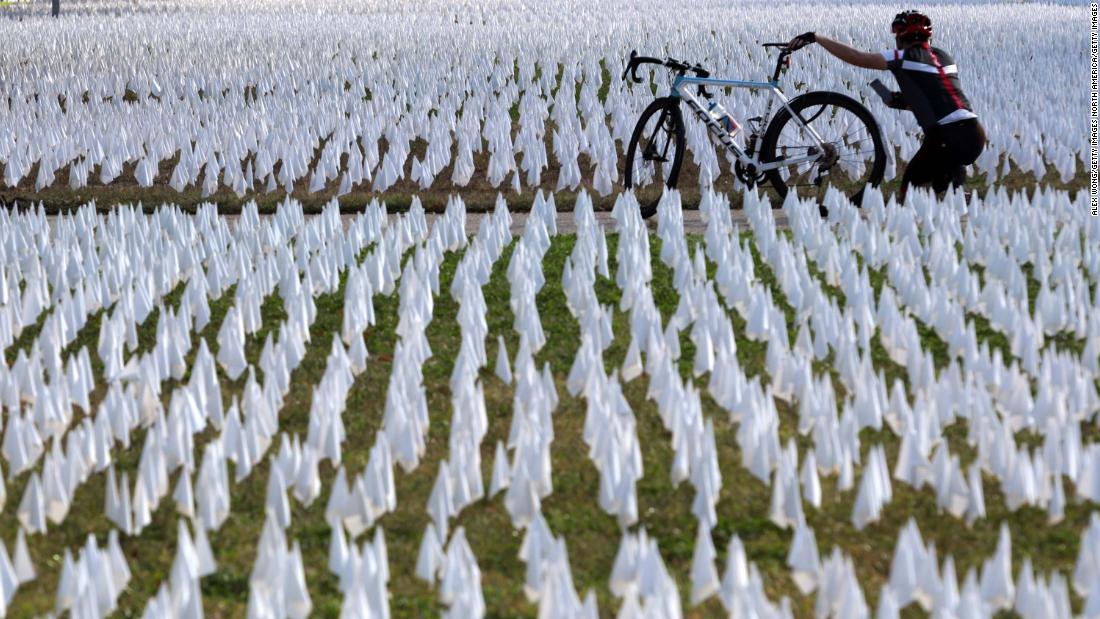 A cyclist takes pictures of a public art project set up on the DC Armory Parade Ground in Washington, DC. An estimated 240,000 flags were planted to represent lives lost to Covid-19. The display, created by local artist Susanne Brennan Firstenberg, was on display for two weeks.