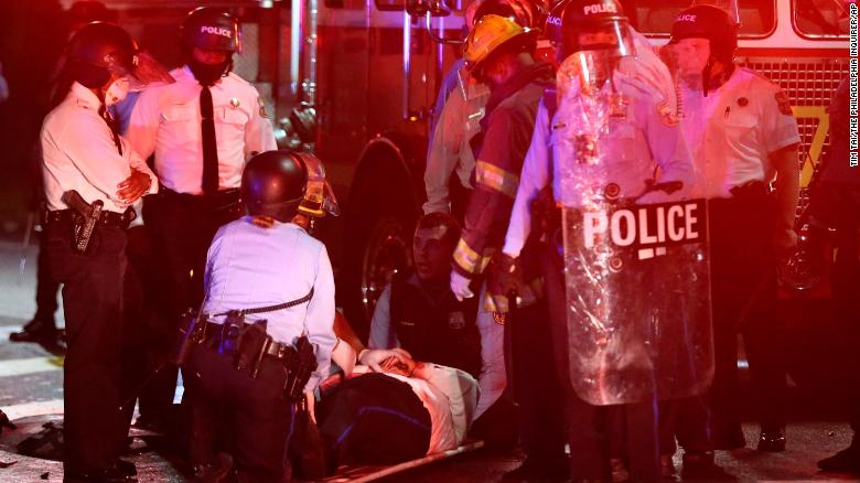 A police officer lies on the ground before being loaded into an ambulance on 52nd Street in West Philadelphia in the early hours of Tuesday, Oct. 27, 2020.