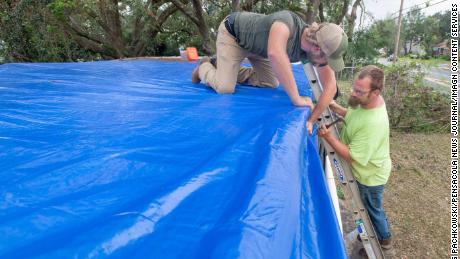 Benjamin Elkins, left, and Jack Beasley install a tarp Tuesday on Eklin&#39;s home in Pensacola, Florida.