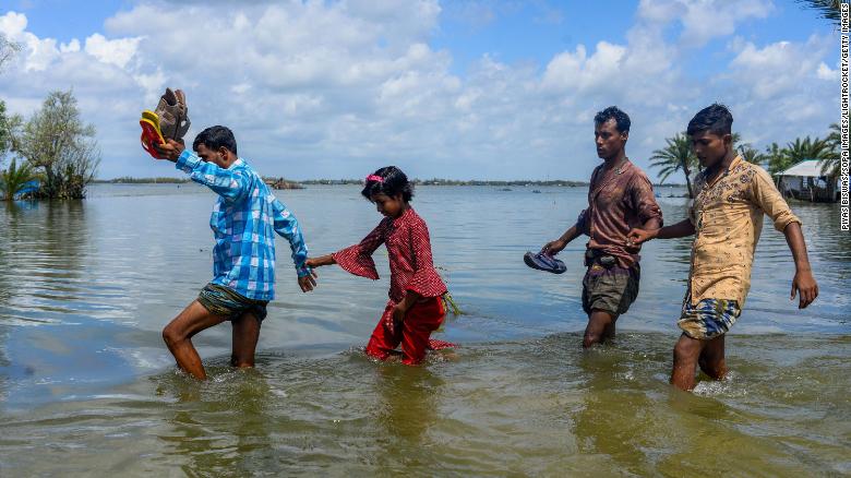 People cross the broken flooded road after the landfall of Cyclone Amphan in Bangladesh. 