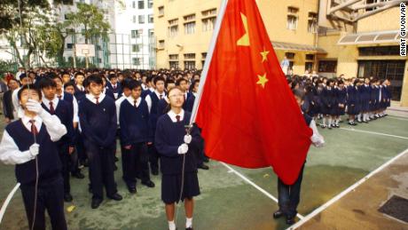 Los estudiantes de la patriótica escuela secundaria Heung To en Hong Kong ven a Cheung Kit-yuk (centro) y Chiu Pak-min (extremo izquierdo) izar la bandera nacional china al son del himno nacional durante una ceremonia en los terrenos de la escuela el viernes 2 de abril de 2004 . 