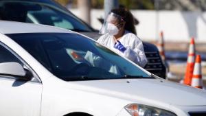 A tester talks to a motorist before administering a swab test at a drive-in, COVID-19 testing site Tuesday, Oct. 27, 2020, in Federal Heights, Colo. Denver will enforce tighter restrictions for restaurants, retail and offices, reducing maximum capacity from 50 percent to 25 percent amid a spiraling rise in cases of the coronavirus in the state in the past month. (AP Photo/David Zalubowski)