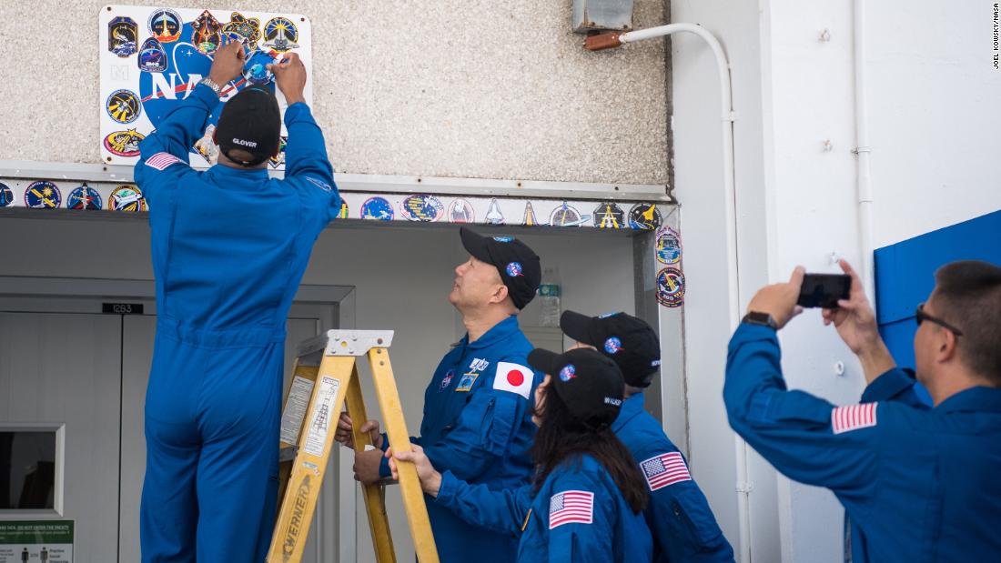 Glover places a Crew-1 mission sticker above the doorway to crew quarters at the Neil Armstrong Operations and Checkout Building as his fellow crewmates look on, November 12 at Kennedy Space Center.