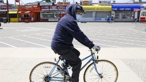 A man wearing a protective mask and gloves cycles past the Boardwalk across from the Hampton Beach State Park in Hampton, N.H., Tuesday, May 19, 2020. Beaches in New Hampshire have been closed since March by state order due to the COVID-19 virus outbreak. (AP Photo/Charles Krupa)