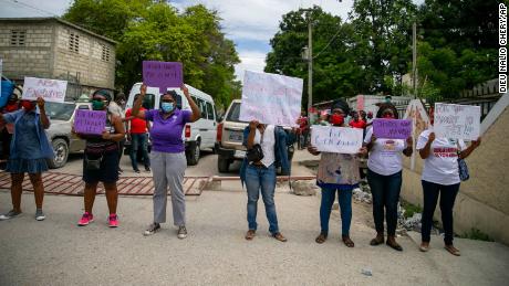 Women hold up signs demanding justice during the hearing of president of the Haitian Football Federation Jean-Bart.