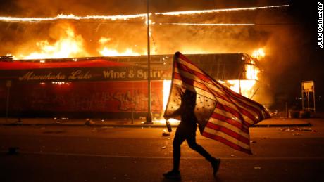 A protester carries an American flag upside down next to a burning building in Minneapolis on May 28. Protesters started rallying across the United States after the death of George Floyd, a Black man who was killed in police custody in Minneapolis.