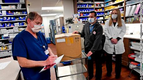 Vail Health Hospital pharmacy technician Rob Brown, left, signs the necessary paperwork to take possession of mock Covid-19 vaccines from courier driver Leo Gomez, center, as pharmacist Jessica Peterson watches over the process in the pharmacy on December 8, 2020, in Vail, Colorado.  