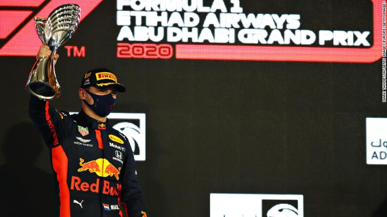Verstappen stands on the podium with his trophy. 