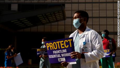 Dr. Lawrence Benjamin wears a face mask and carries a sign in support of resident physicians, interns and fellows at UCLA Health as they protest for improved Covid-19 testing and workplace safety policies outside of UCLA Medical Center in Los Angeles, California, December 9, 2020. (Photo by Patrick T. Fallon / AFP) (Photo by PATRICK T. FALLON/AFP via Getty Images)