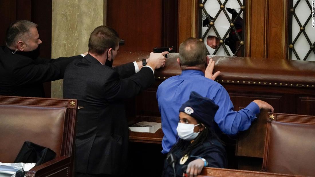 Law enforcement officers point their guns at a door that was vandalized in the House chamber after the Capitol was breached.