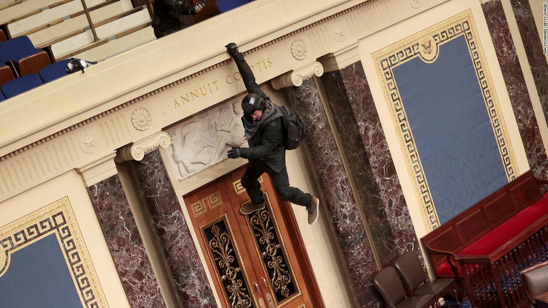 A rioter hangs from a balcony in the Senate chamber.