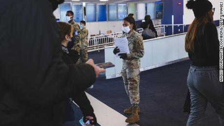 A member of the New York Army National Guard hands out health forms to travelers wearing protective masks at LaGuardia Airport on December 24.