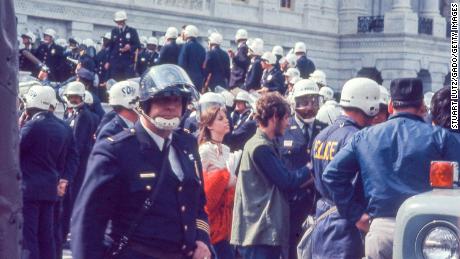 Police in riot gear surround protesters in hippie attire during the 1971 May Day protests.