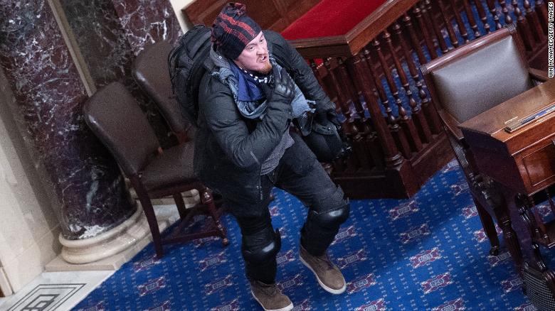 Man seen hanging off Senate balcony and sitting in Vice President’s chair during Capitol riot is in custody
