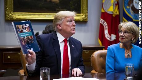 Trump holds up the Federal Commission on School Safety report while Betsy DeVos, U.S. secretary of education, right, listens. 