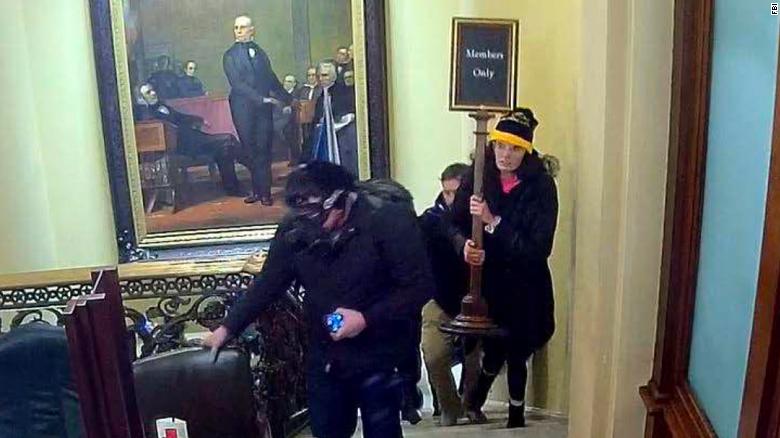 In an image taken from surveillance video, Gracyn Courtright is seen walking up the steps near the Senate Chamber carrying a &quot;Members Only&quot; sign.