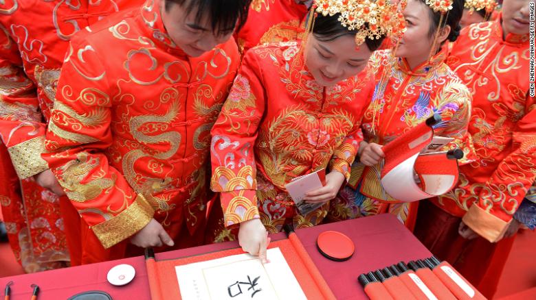 Пара отмечает отпечатки пальцев на церемониальной каллиграфии во время традиционной групповой свадьбы в Чанше, Китай.