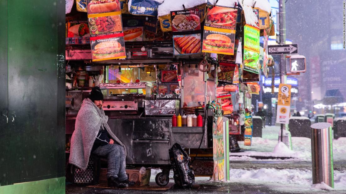 A food-cart vendor is wrapped in a blanket as snow falls in Times Square on Monday.