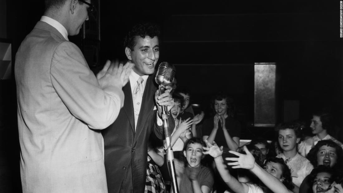 Bennett performs on a stage in Cleveland as local DJ Bill Randall applauds and young girls scream in the audience. Bennett had a string of hits in the early to mid-1950s, including chart-toppers &quot;Because of You&quot; and &quot;Rags to Riches.&quot;