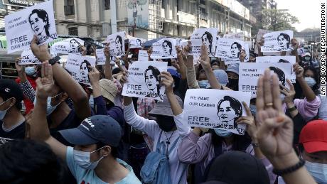 Demonstrators hold placards showing the image of Aung San Suu Kyi as they flash the three-finger salute in Yangon on February 7, 2021.