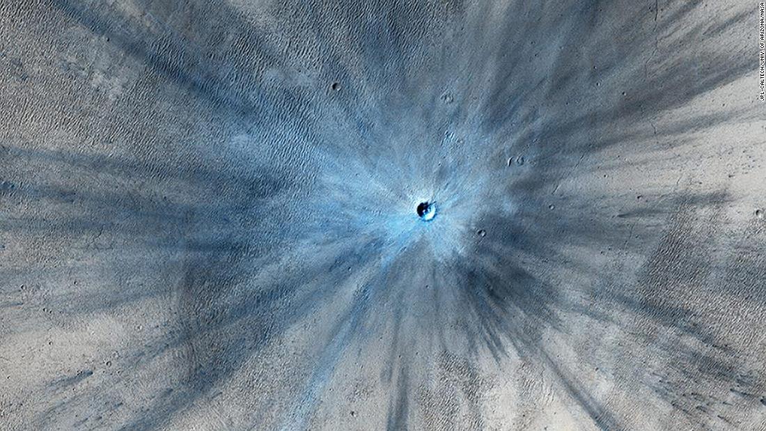 A dramatic, fresh impact crater dominates this image taken by the HiRISE camera in November 2013. The crater spans approximately 100 feet and is surrounded by a large, rayed blast zone. Because the terrain where the crater formed is dusty, the fresh crater appears blue in the enhanced color of the image, due to removal of the reddish dust in that area.