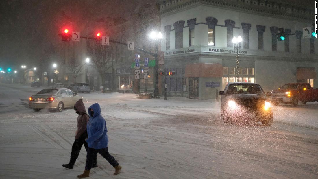 Two women cross Main Street as snow falls in Bowling Green, Ohio, on Monday.