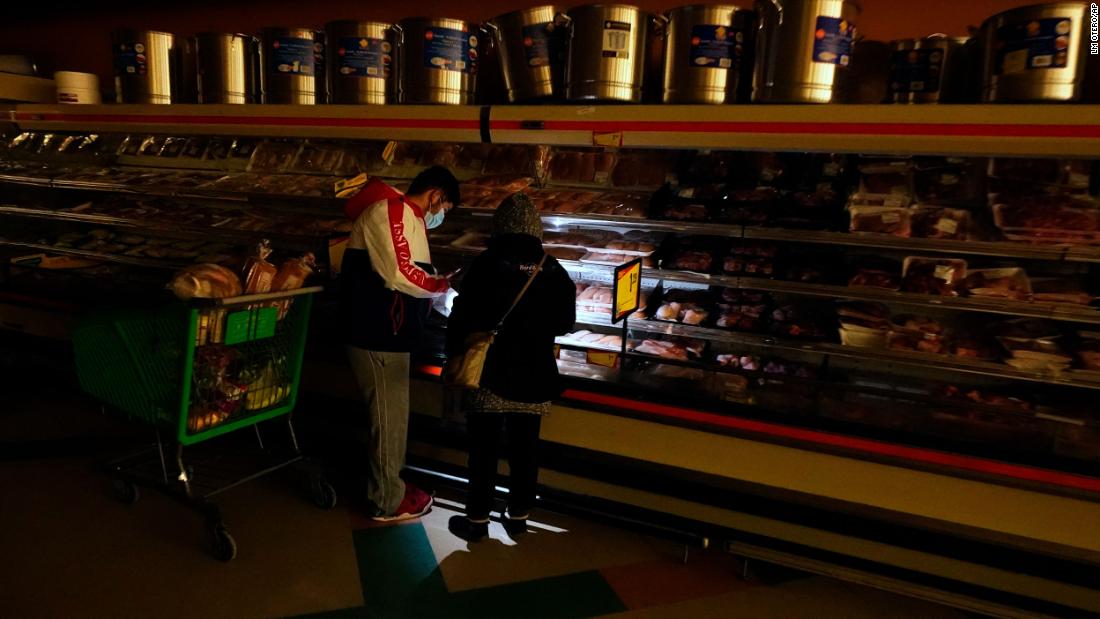 Customers use light from a cell phone as they shop for meat at a grocery store in Dallas on Tuesday. Even though the store lost power, it was open for cash-only sales.