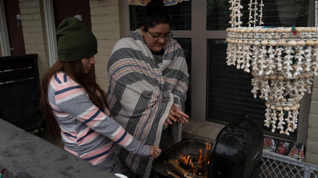 Karla Perez and Esperanza Gonzalez warm up by a barbecue grill after their power was knocked out in Houston on Tuesday.