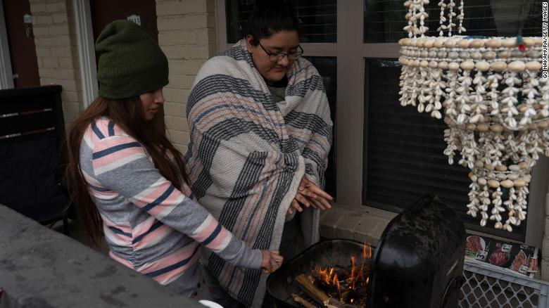 Karla Perez and Esperanza Gonzalez warm up by a barbecue grill during power outage caused by the winter storm on February 16.