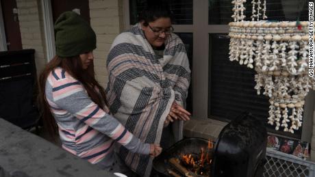 Karla Perez and Esperanza Gonzalez warm up by a barbecue grill during power outage Tuesday in Houston.