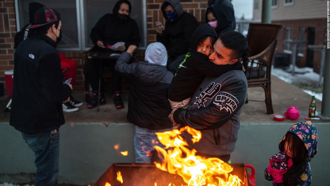 Eric Traugott warms up his young son, Eric Jr., beside a fire made from a discarded wooden armoire outside of their apartment in Austin on Wednesday.
