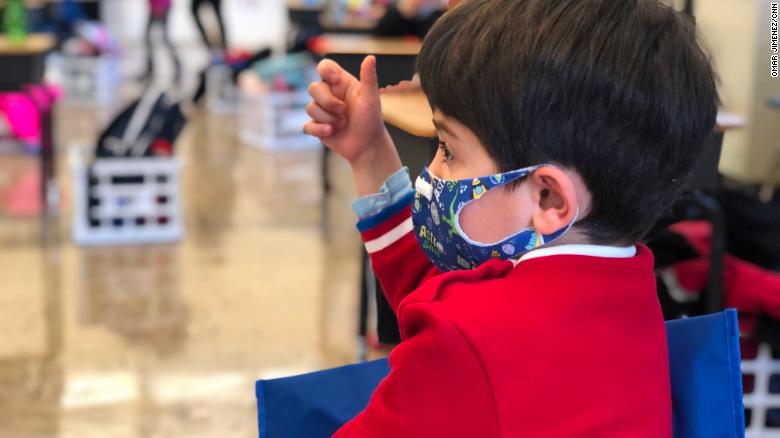 A masked kindergarten student at Hawthorne Scholastic Academy in Chicago raises his hand during his first day back in the classroom.