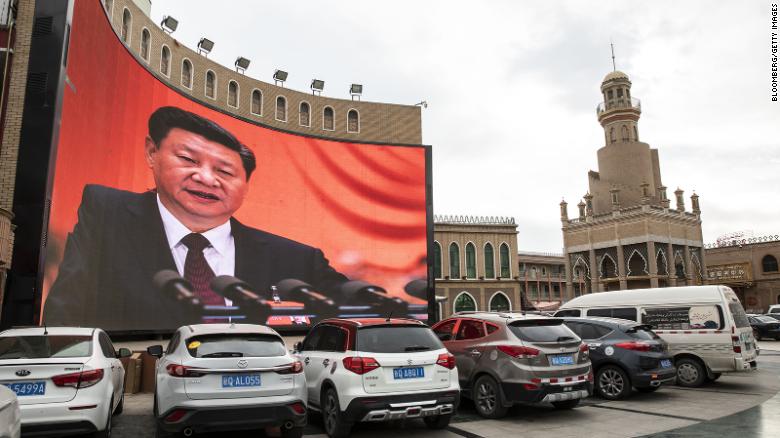 Vehicles stand in a parking lot as a large screen shows an image of Chinese President Xi Jinping in Kashgar, Xinjiang autonomous region, China, on Thursday, November 8, 2018.