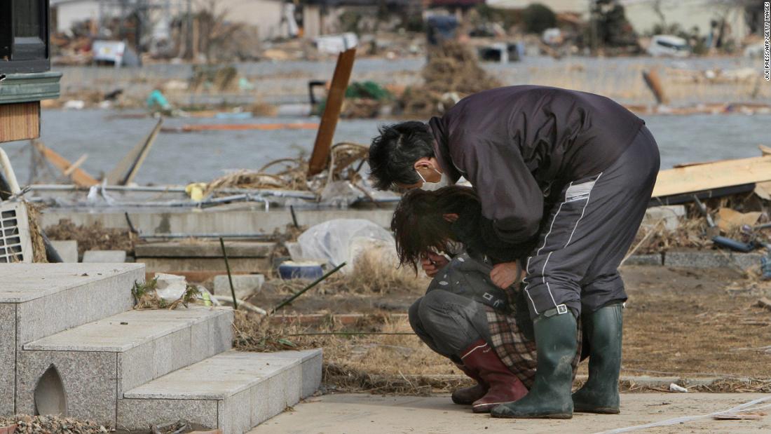 A man comforts a woman as she cries in front of her damaged home in the town of Watari in Miyagi prefecture.