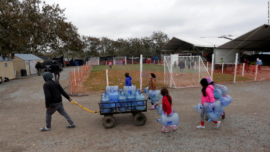 Migrants seeking asylum in the United States carry empty water jugs at a camp in Matamoros, Mexico, on February 18.