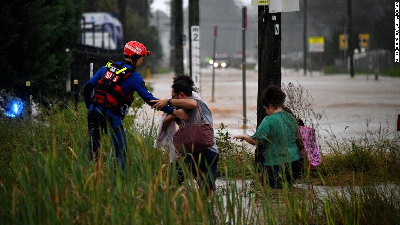 A rescue worker helps residents cross a flooded road in western Sydney on March 20
