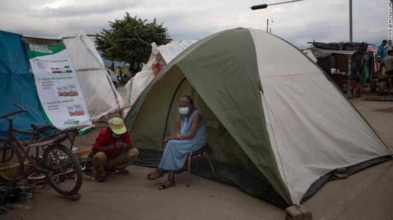 An elderly woman sits outside a tent in Lima, Honduras, where she lives after losing her home in last year&#39;s hurricanes Eta and Iota. Devastation from the storms and the economic damage of the Covid-19 pandemic have added to the forces that drive Hondurans to migrate.