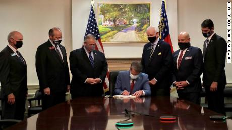 Georgia Gov. Brian Kemp signs S.B. 202 on Thursday, March 25. Kimberly Wallace says the painting behind him depicts the plantation on which her family members worked, going back to slavery.