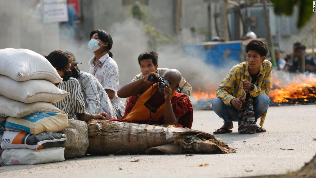 A Buddhist monk uses binoculars as he squats behind a road barricade with others in Mandalay, Myanmar, on March 22.