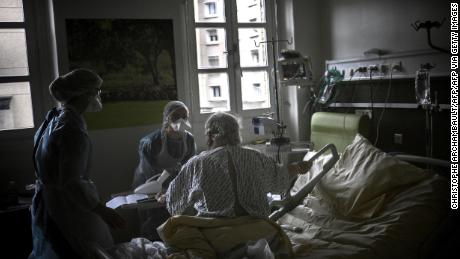 Nurses help a Covid-19 patient sitting in his bed, in a room, of the pneumology unit of the AP-HP Cochin hospital, in Paris on March 18, 2021.