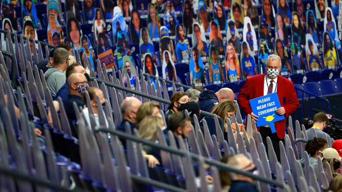 An usher at the Final Four holds a sign that reads &quot;please wear face coverings.&quot; The fans were spread out with the help of cardboard cutouts.