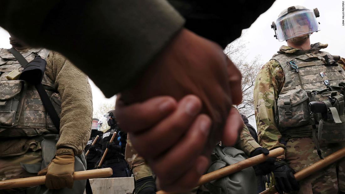 Members of the National Guard watch as protesters hold hands during a rally outside the Brooklyn Center Police Department on Monday.