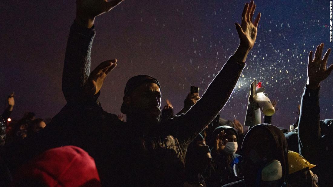 Protesters raise their hands in front of the Brooklyn Center Police Department on Monday.