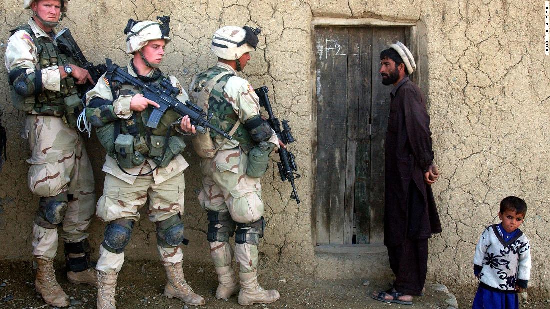 A man and his son watch US soldiers prepare to sweep their home in southeastern Afghanistan in November 2002.